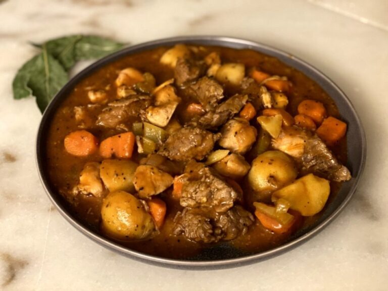 chicken and beef stew with carrots, onions, potatoes, garlic, on gray plate with bay leaves