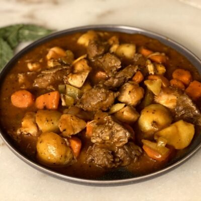 chicken and beef stew with potatoes, carrots, oninos, celery in sauce in a gray plate