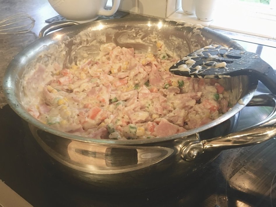 adding the sliced ham and frozen peas, carrots, corn, onions into the creamy sauce. 
