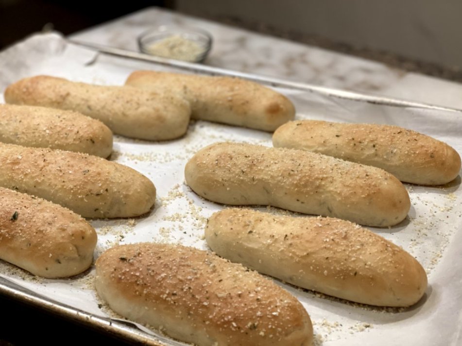 garlic rosemary breadsticks on parchment paper with garlic salt on a baking sheet