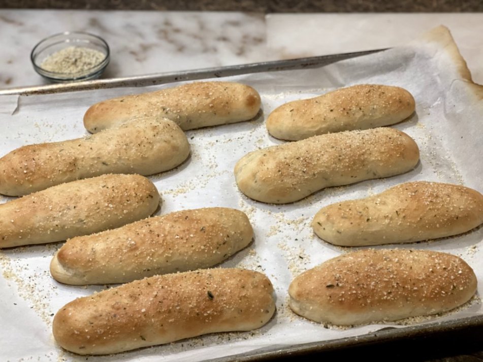 Thick fluffly garlic rosemary breadsticks sprinkled with garlic salt on a large metal baking sheet with parchment paper. 
