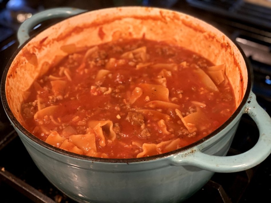 lasagna noodles in a sausage tomato soup in a blue dutch oven