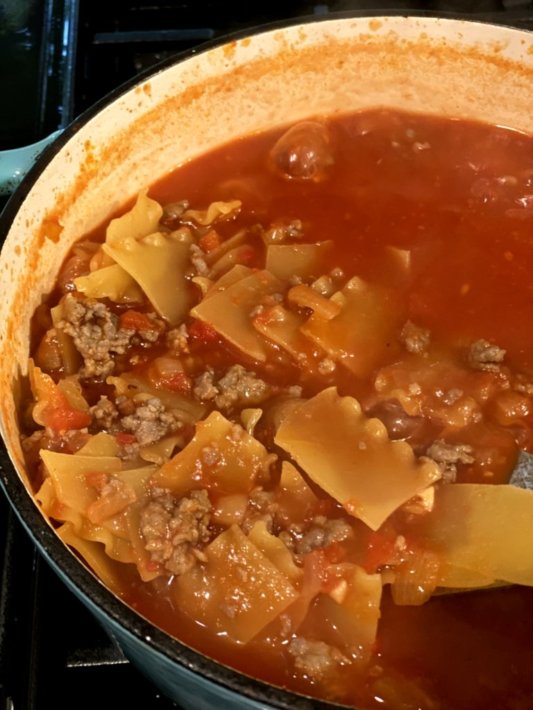 broken lasagna noodles in a sausage tomato based soup in a blue cast iron dutch oven