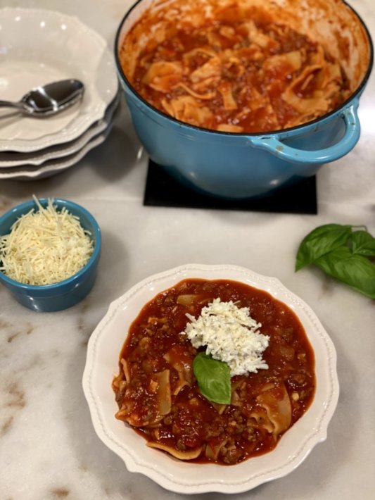 hearty lasagna soup in a white dish with red napkins, cheese on top and a garlic breadstick on the side. soup in a blue dutch oven with parmesan cheese on the side.