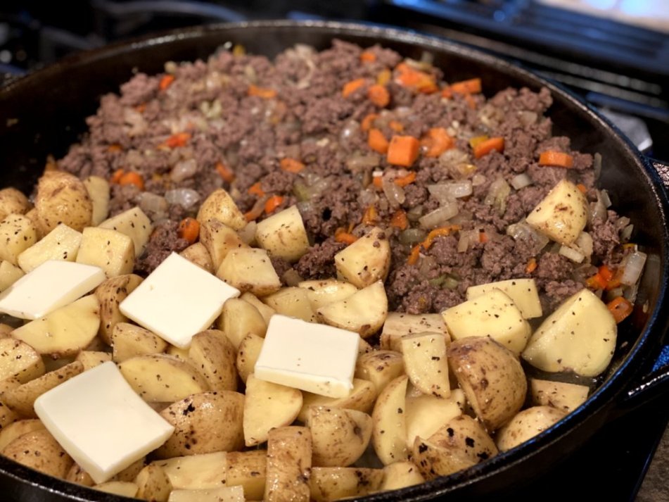 browned ground beef with cooked vegetables, potatoes, and butter in a skillet. 