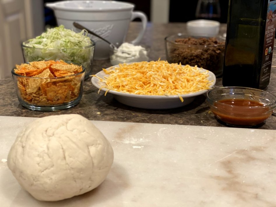 homemade pizza crust with bowls of our favorite toppings for the tasty taco pizza.