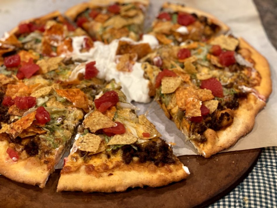 easy taco pizza with taco meat, cheese, sour cream and tortilla chips on a pizza stone