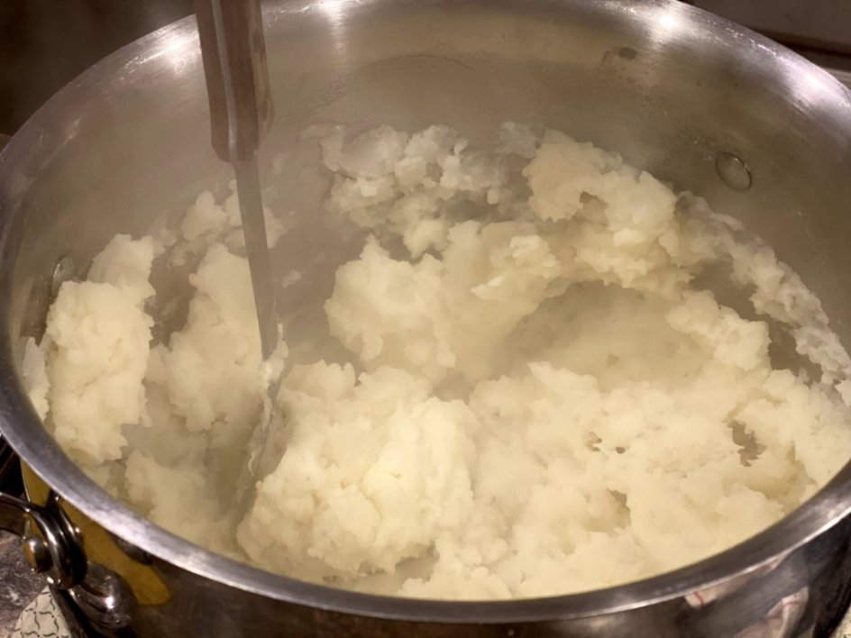 mashing boiled potatoes in a large pot