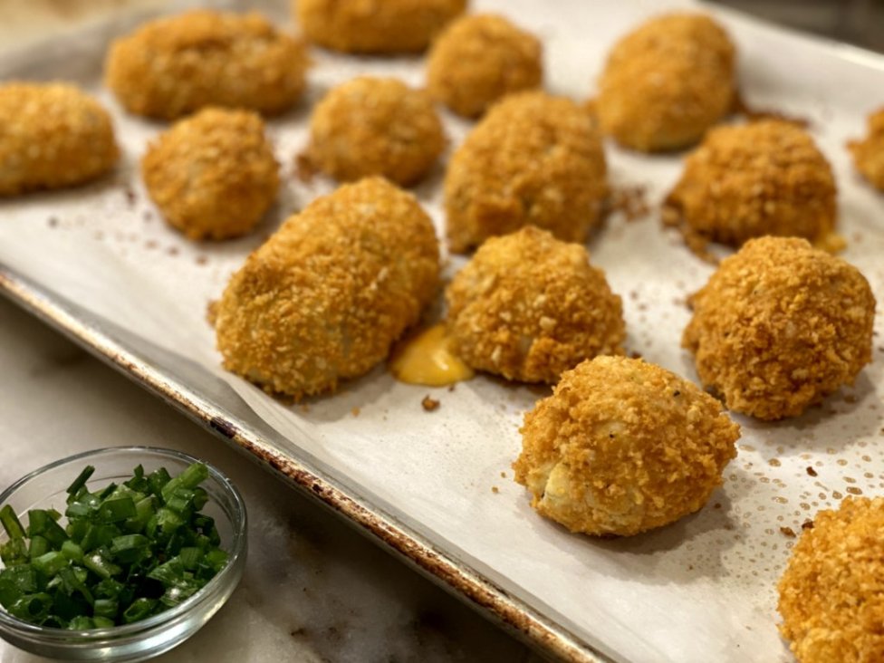 Cheesy Chicken Baked Croquettes fresh out of the oven on a baking sheet with parchment paper and chopped green onions on the side