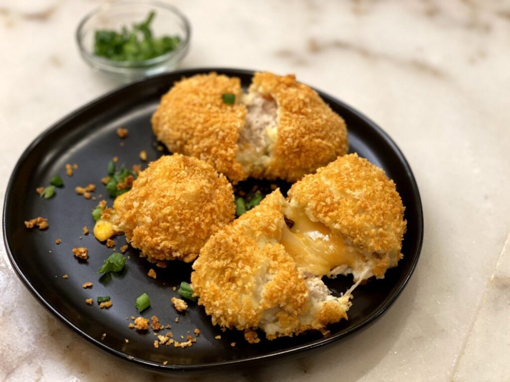 Cheesy Chicken Baked Croquettes on a black plate with chives and green onions