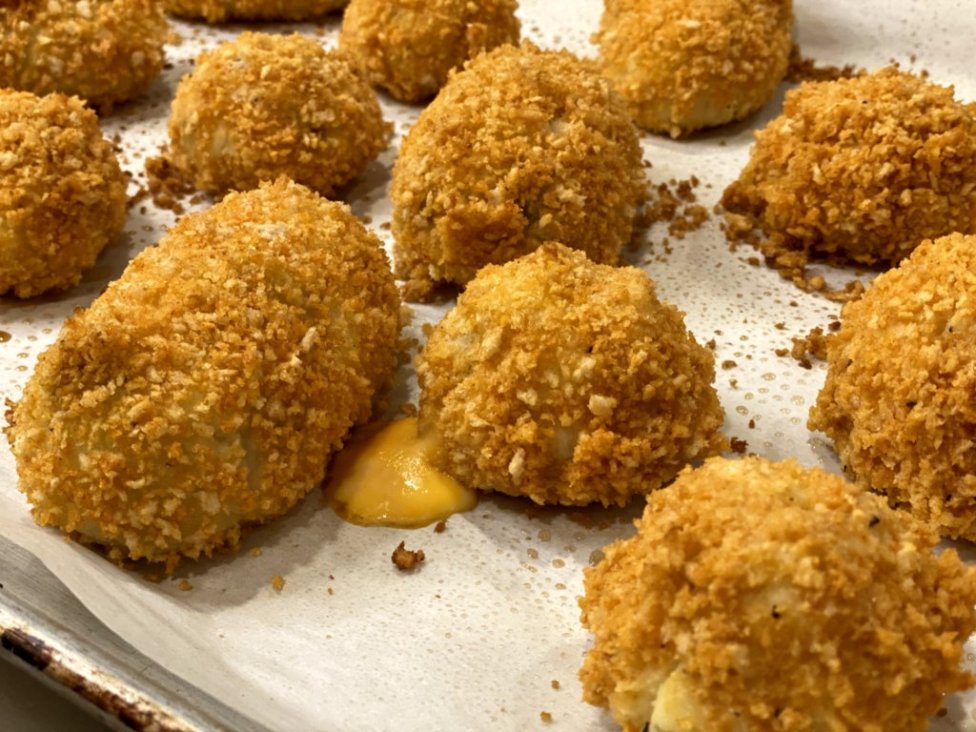 Cheesy Chicken Baked Croquettes out of the oven on parchment paper with cheese oozing out.
