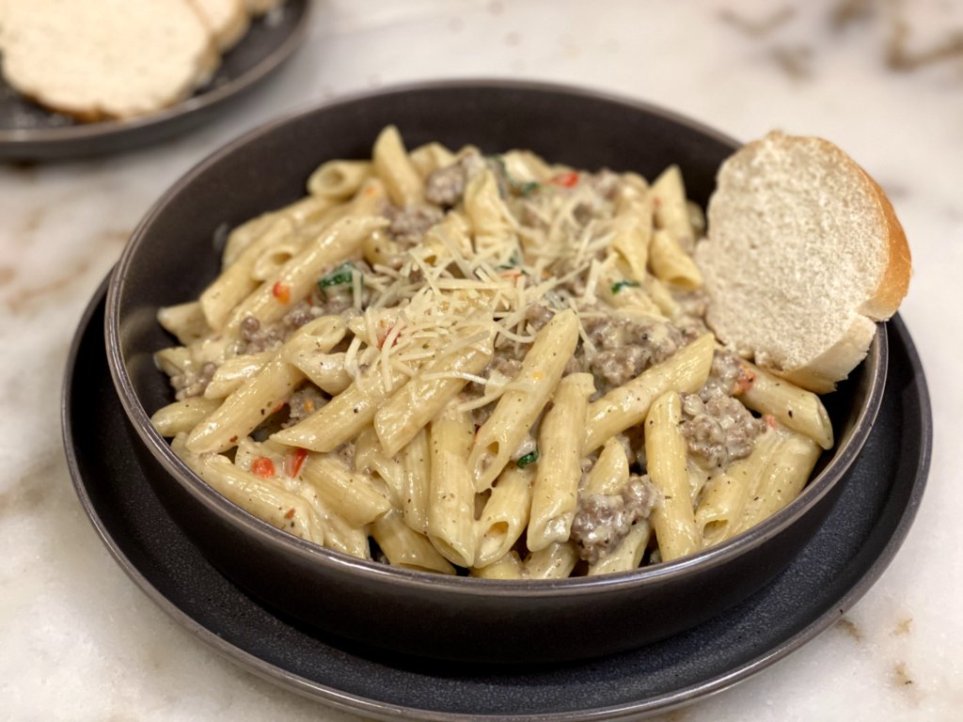 creamy Italian sausage pasta recipe served on a black plate with french bread and topped with sprinkles of parmesan cheese and parsley.