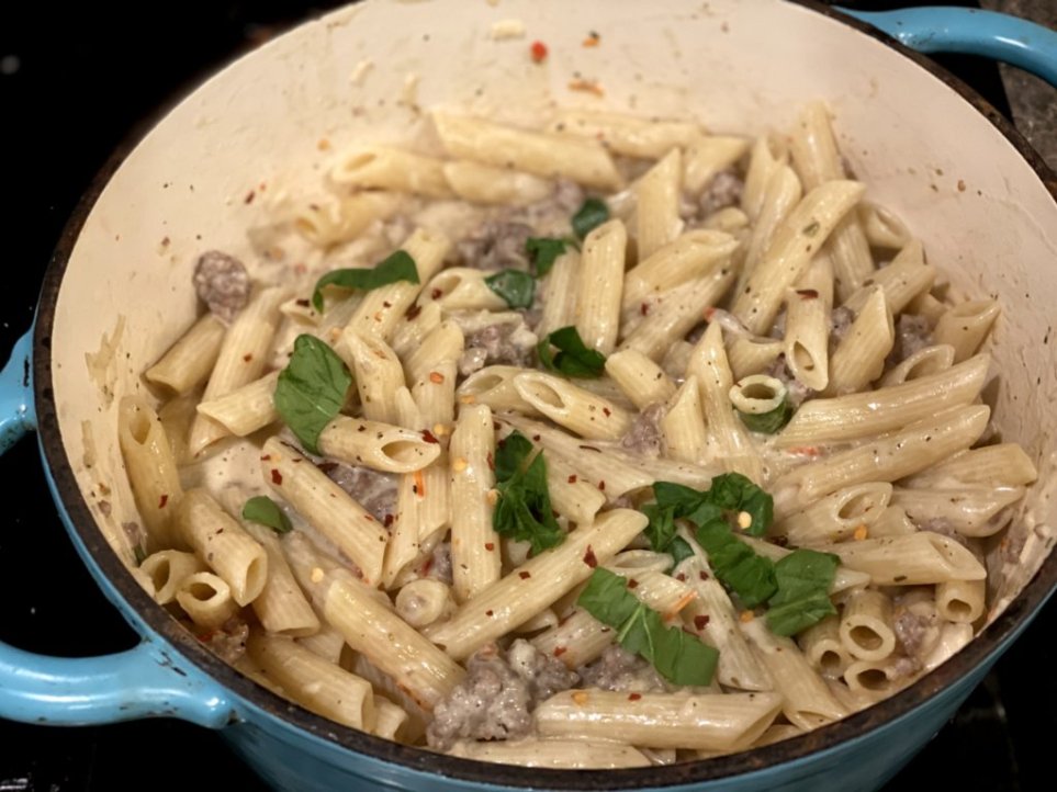 chopped spinach added to creamy Italian sausage pasta in a blue dutch oven. 