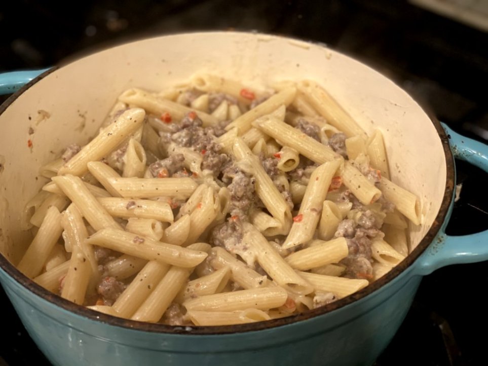 dried red pepper flakes added to creamy italian sausage pasta in a blue pot. 