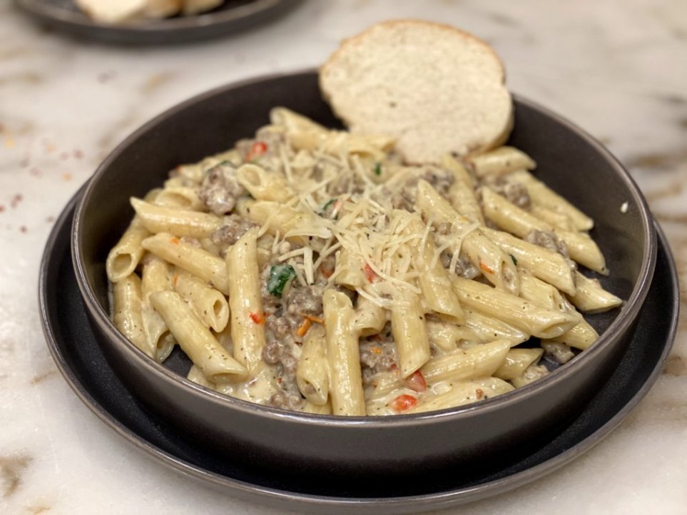 creamy Italian sausage pasta recipe served on a black plate with french bread and topped with sprinkles of parmesan cheese and parsley.