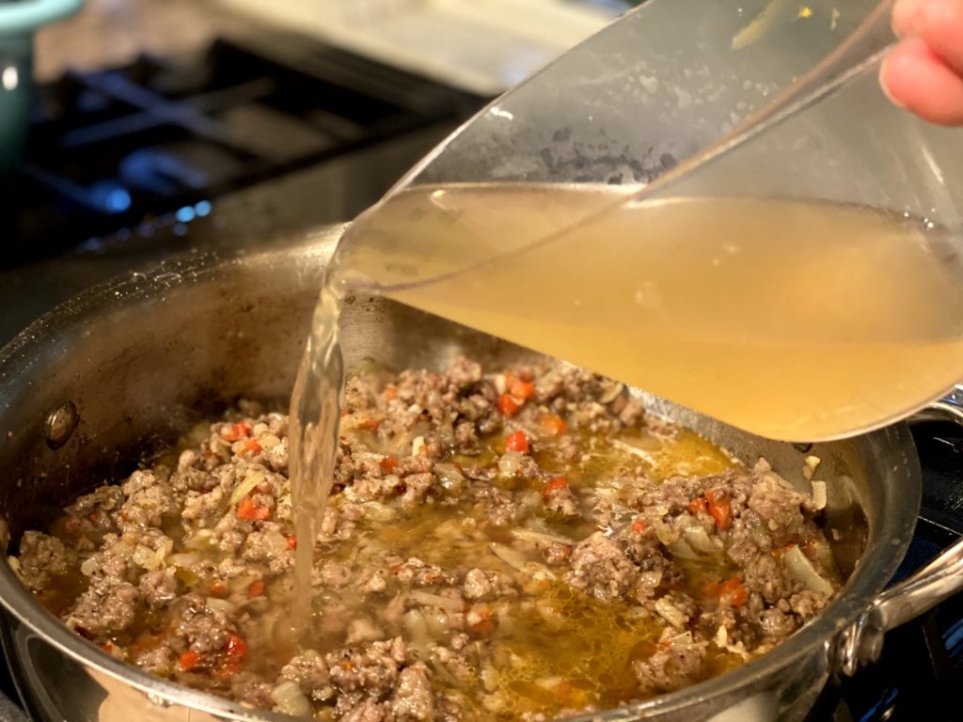 Pourng chicken broth into cooked Italian sausage and vegetables