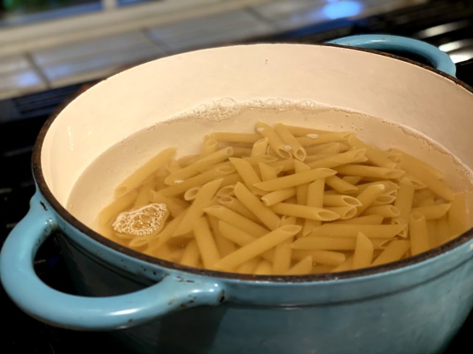 boiling penne pasta in a blue cast iron dutch oven 