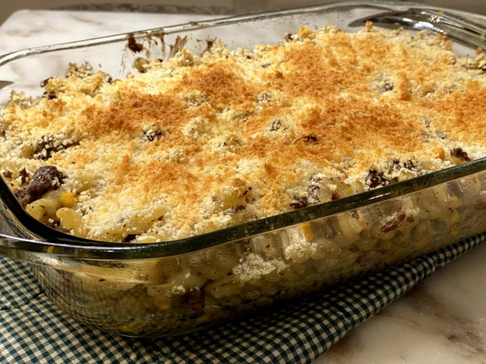 cooked ground beef with corn, sour cream, milk, cream of chicken soup and pasta noodles on the side in a glass baking dish on a green and white hot pad