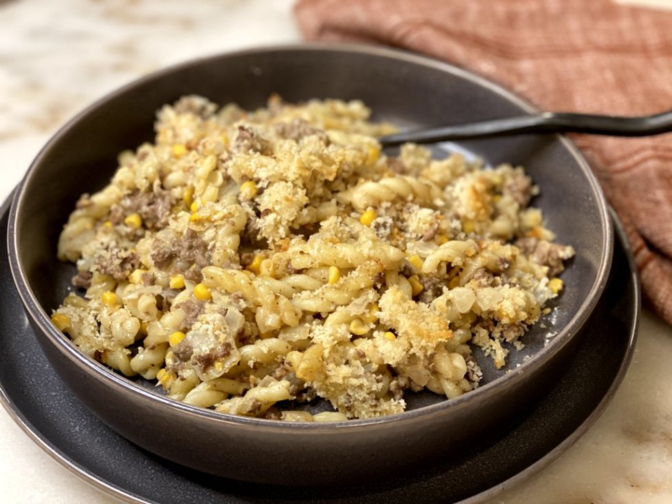 Hamburger Noodle Bake - cooked ground beef with corn, sour cream, milk, cream of chicken soup and pasta noodles on the side served in a gray dish with a red napkin on the side