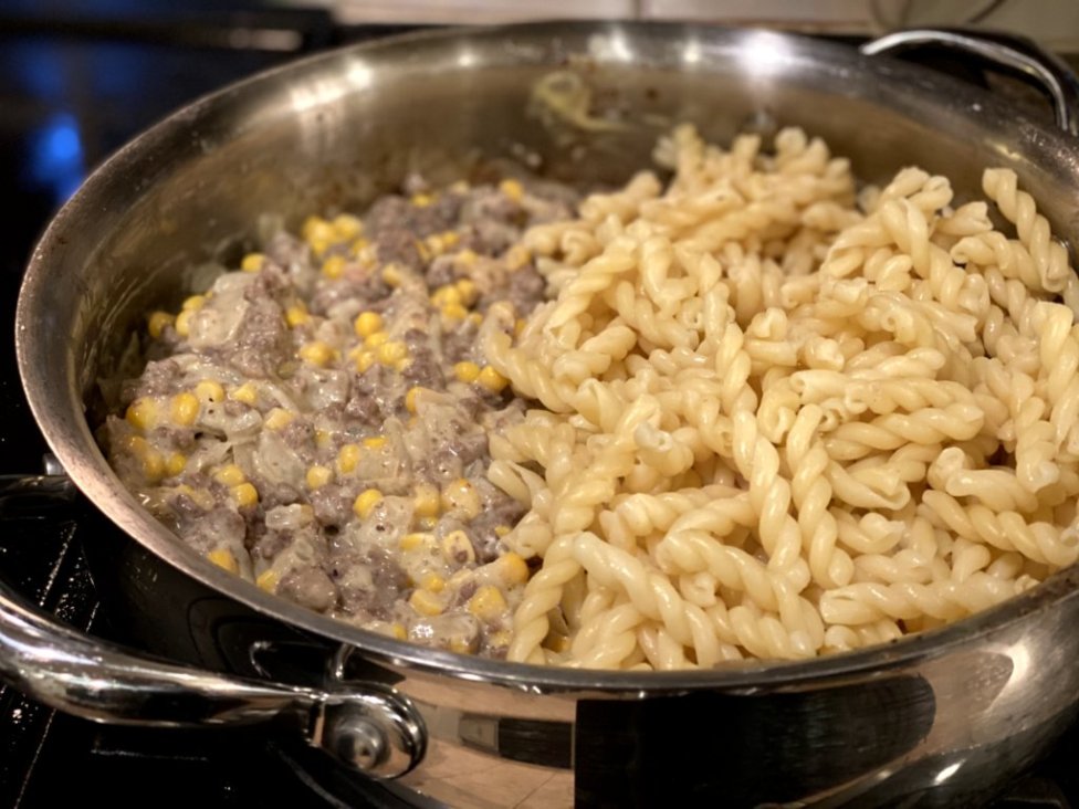 cooked ground beef with corn, sour cream, milk, cream of chicken soup and pasta noodles on the side in a large skillet. 
