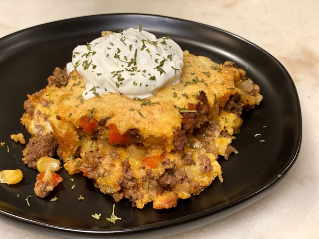 sweet and spicy tamale pie tamale casserole with corn muffin mix, ground beef, red bell peppers, onions, creamed corn, seasonings, topped with sour cream and dried parsley.