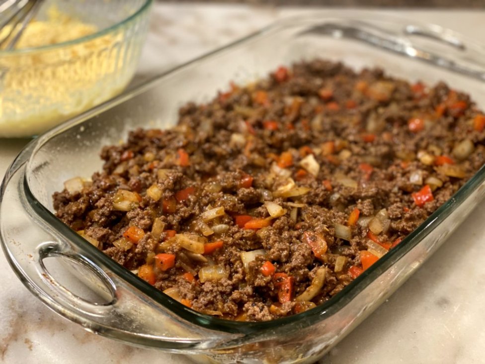 preparing tamale casserole or tamale pie with ground beef mixture and vegetables. 