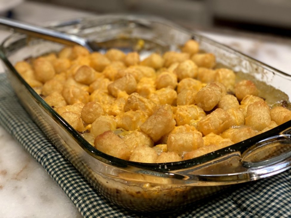 baked and crispy - delicious tater tot casserole hotdish with sprinkled melted cheddar cheese in a glass baking dish with a serving spoon.