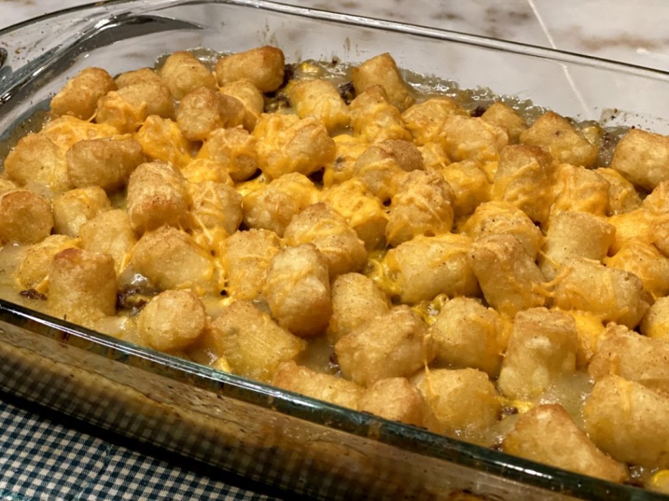 baked crispy tater tots with shredded cheddar cheese in a glass baking dish 