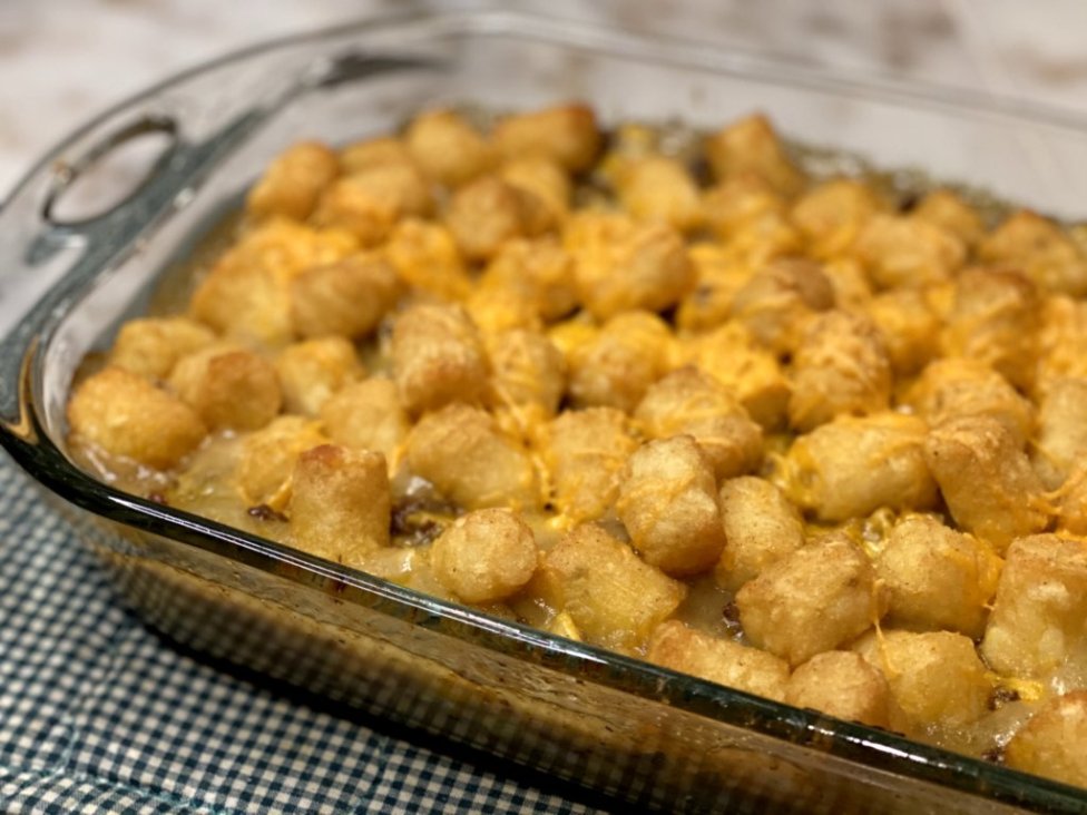 tater tot casserole hotdish covered in cheddar cheese in a glass baking dish. 