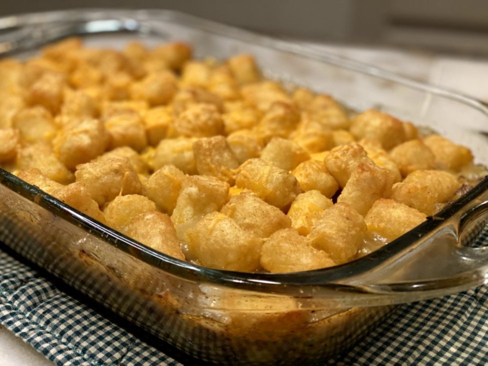 Delicious tater tot hotdish in a glass baking dish on a green and white checkered hotpad.