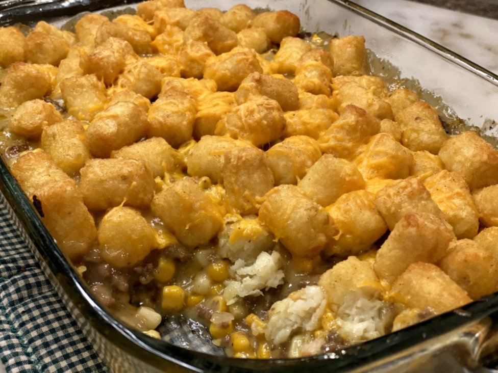 baked delicious tater tot casserole hotdish with cheddar cheese melted on the top with corn and ground beef in the image. 