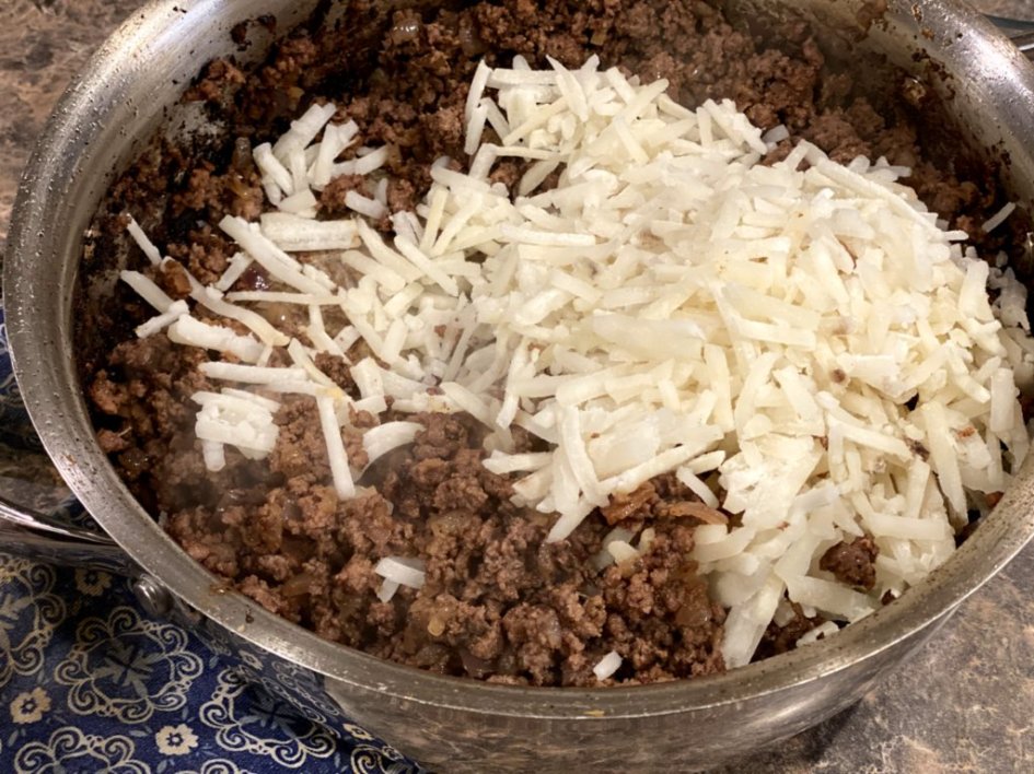 ground beef and frozen hash browns mixed together in a skillet. 