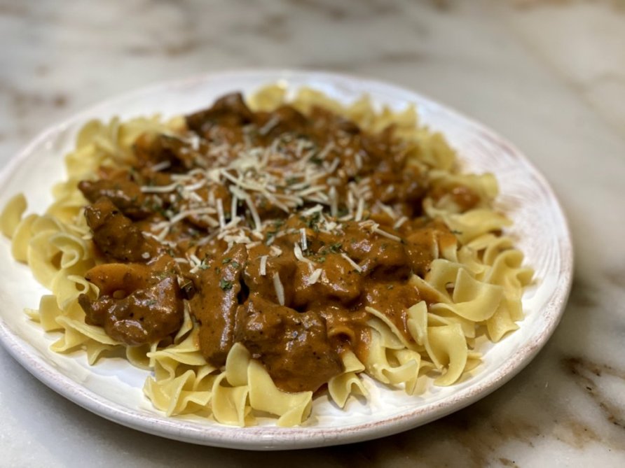 Coogan's Steak stroganoff with noodles, grated parmesean and parsley on a white plate