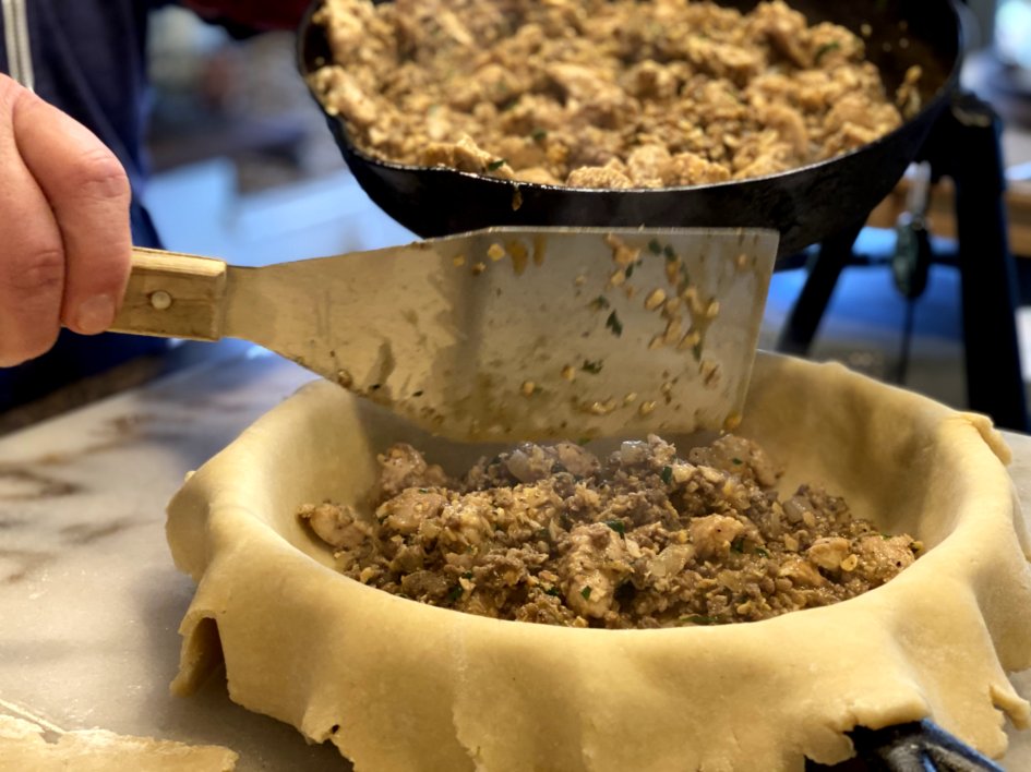 scooping filling inside the pie crust in a cast iron skillet