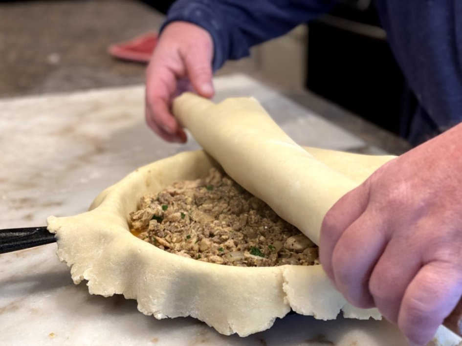 rolling the second pie crust over the filling of the savory chicken pork pie. 