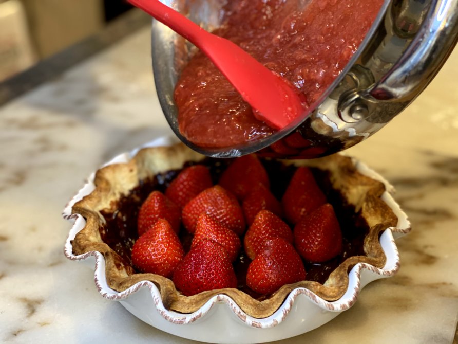 Pouring strawberry glaze over fresh strawberry pie. 