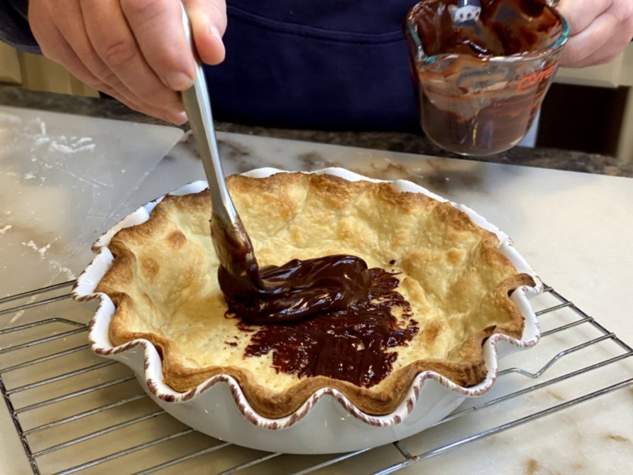 brushing chocolate sauce on the bottom of a baked pie crust