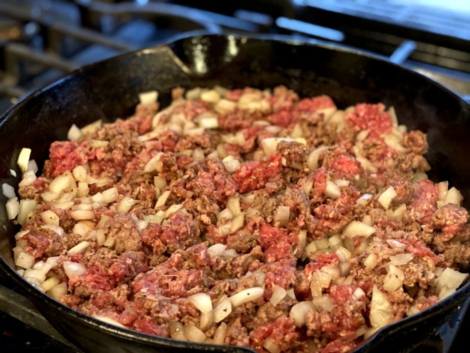 browning ground beef with onions in a black cast-iron skillet