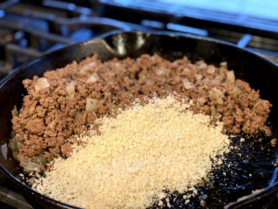 adding panko bread crumbs to browned ground beef in a skillet