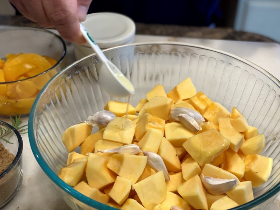 adding olive oil to a bowl of garlic and cubed acorn squash