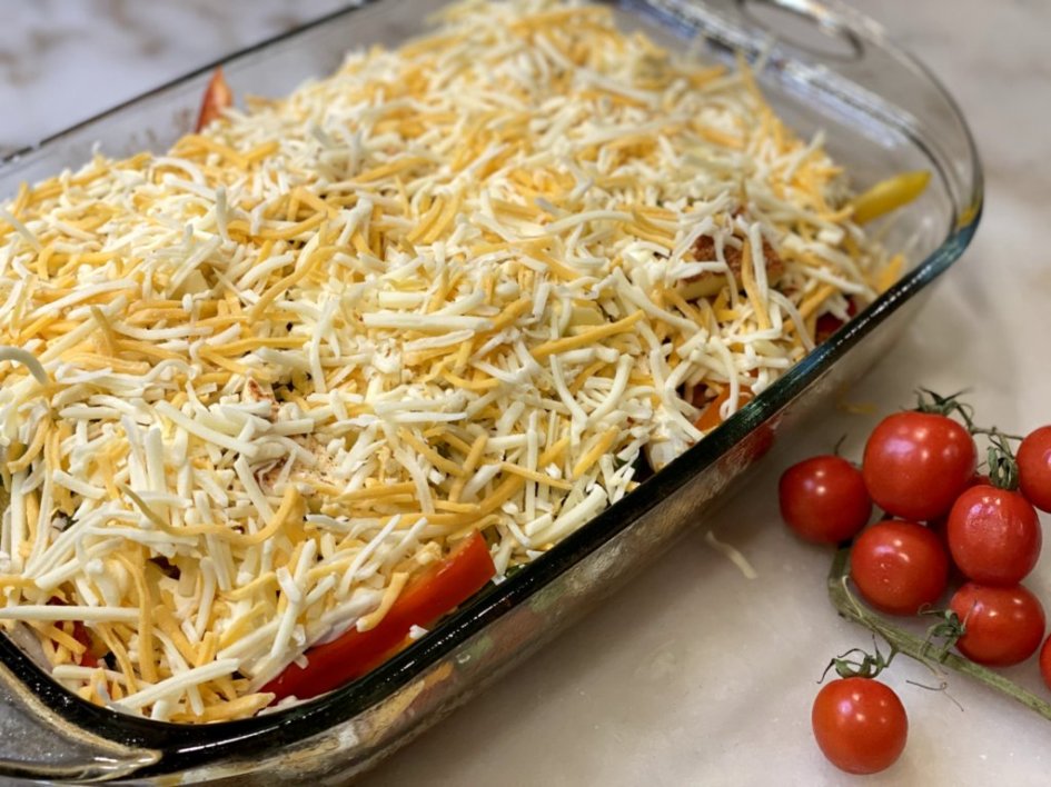 chicken fajita casserole sprinkled with shredded mexican cheese with tomatoes on the side
