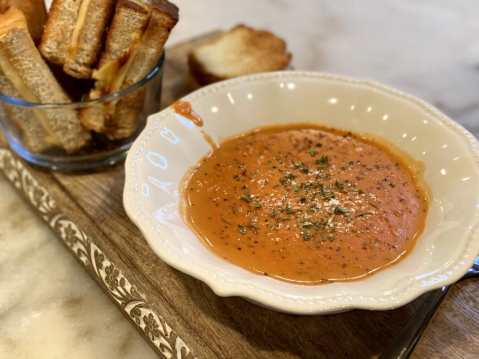 tomato soup in a white bowl with grilled cheese sticks on the side.