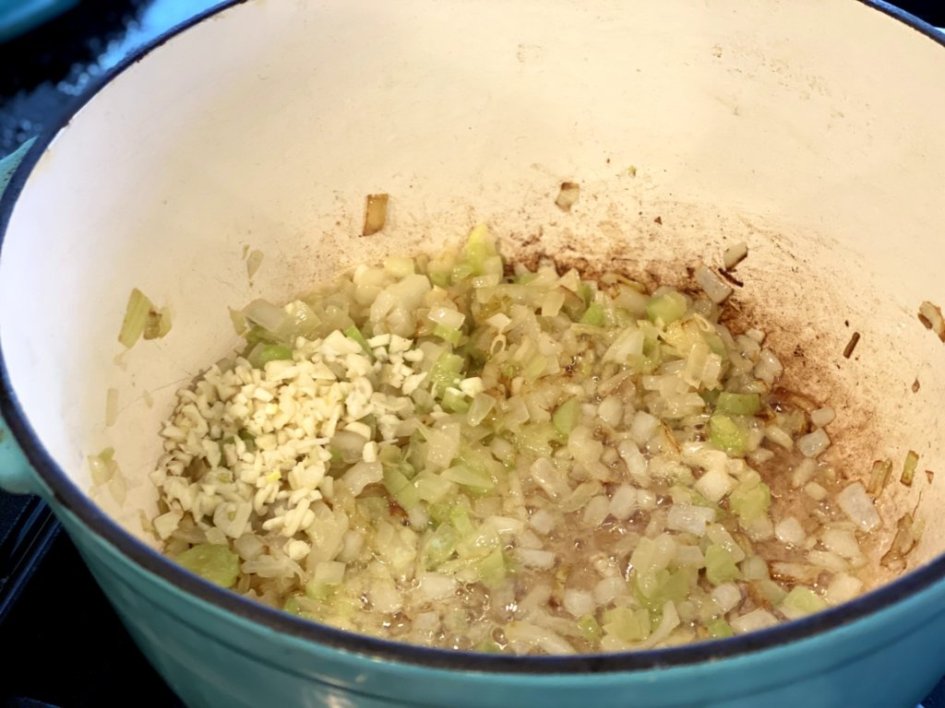 adding garlic to the celery and onions in a blue dutch oven pot.
