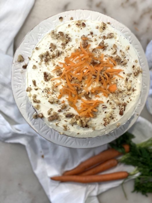 Carrot cake with cream cheese frosting, sprinkled with crushed walnuts, pecans and carrots. 