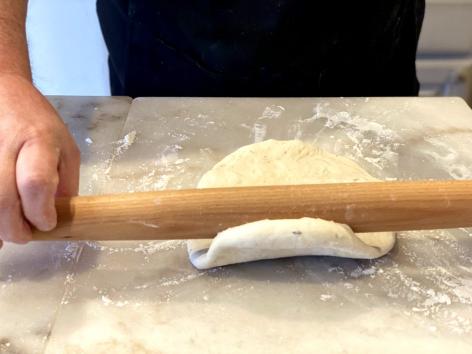 Rolling out the bread dough with a rolling pin and floured surface. 