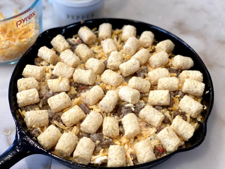 adding tater tots over the top of the sausage and tots breakfast casserole filling