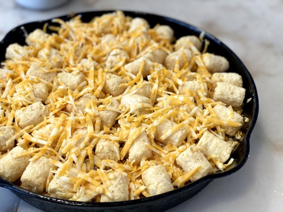tater tots and shredded cheese in the cast iron skillet ready for baking