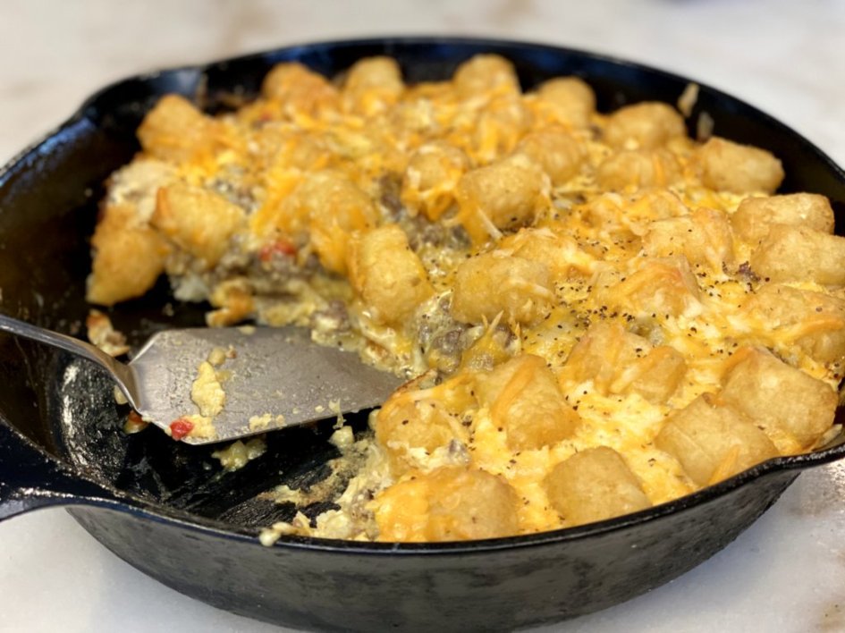 breakfast casserole with tater tots and sausage recipes is ready to serve in a cast-iron skillet