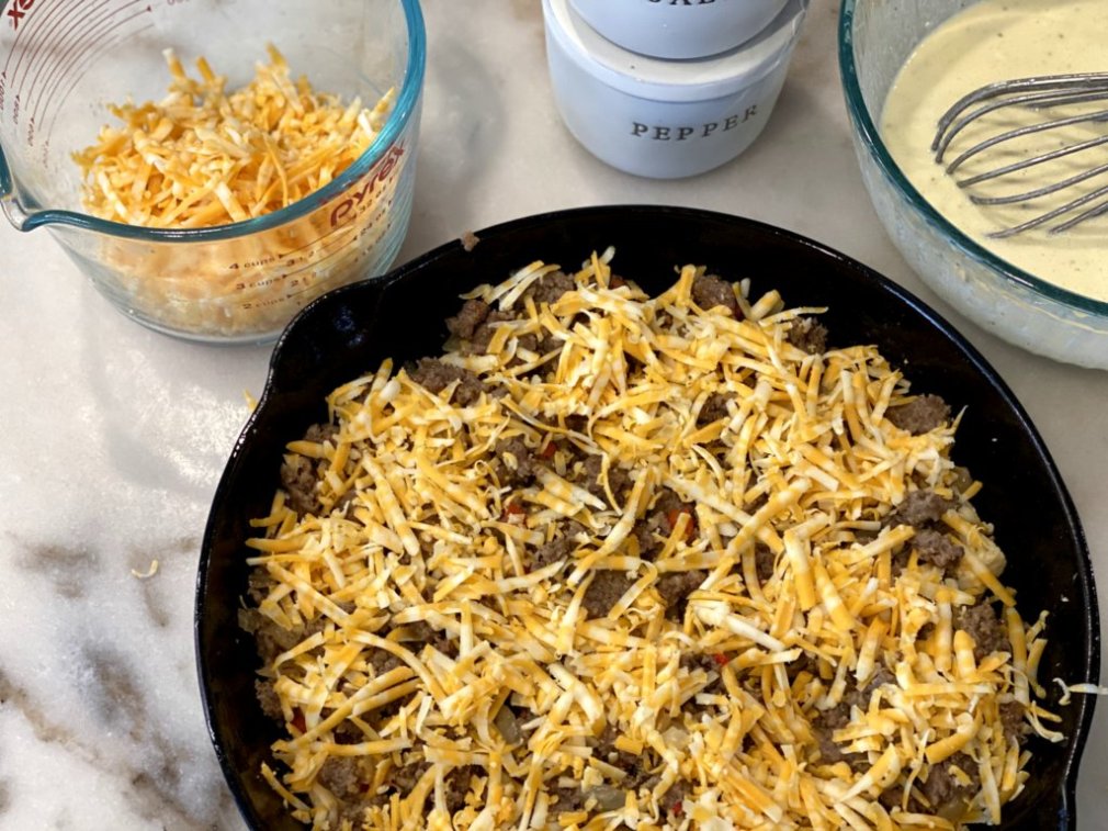 adding shredded cheddar cheese to the casserole in a cast iron skillet
