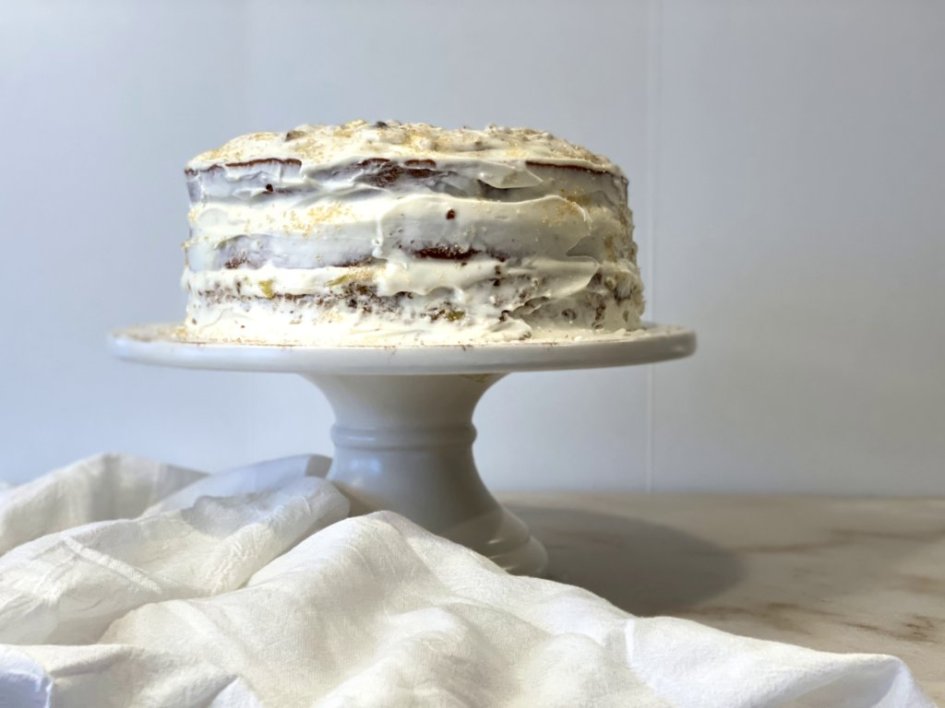 Hummingbird Cake frosted with cream cheese icing on a white cake stand. 